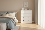 White 4-drawer dresser with black square handles styled in modern bedroom with natural lighting